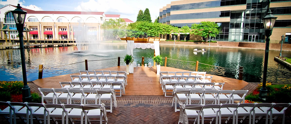 Outdoor shoot of Hilton Charlotte University Place before the wedding with white chairs and flowers by the water.